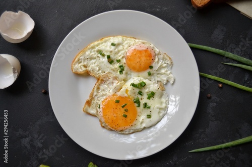 Tasty breakfast. Food on the table. Food on a black concrete decorative background. Fried eggs in a white plate. Eggs, green onions, brown bread, cucumbers.
