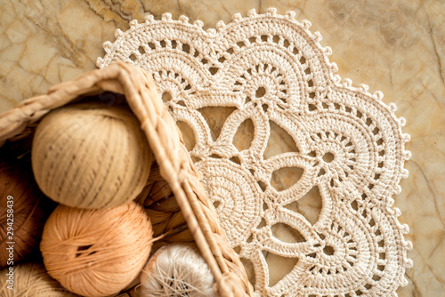 threads, crocheted round napkin. White napkin like a flower. on a marble light background. Balls of thread in a wicker box.cozy home and handmade concept