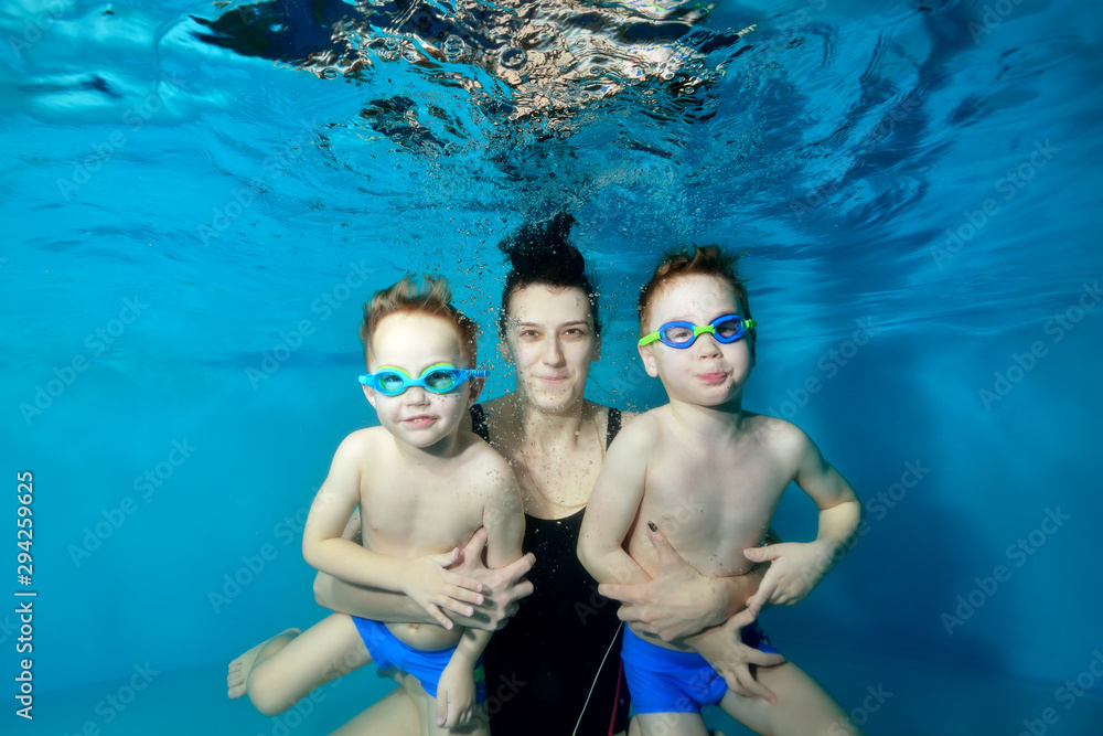 Family: a mother and two young boys swim and pose underwater in the pool. They hug and look at the camera. Children in glasses for swimming. Portrait. Family entertainment. Underwater photography