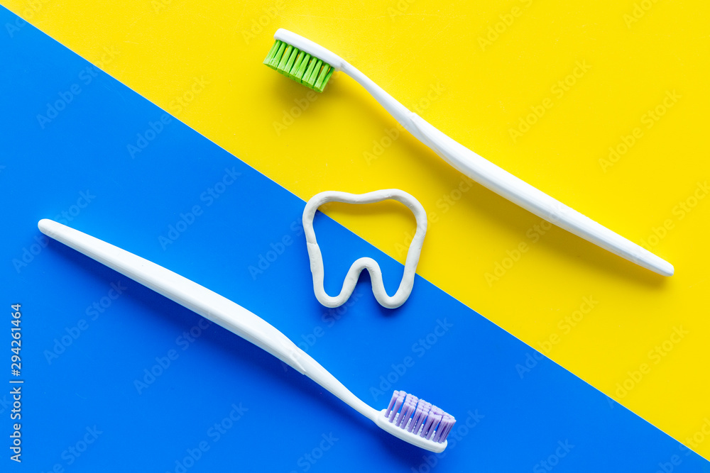 Teeth brushing concept. Tooth drawn with toothpaste near toothbrushes on yellow and blue background top view Teeth brushing concept. Tooth drawn with toothpaste near toothbrushes on yellow and blue background top view