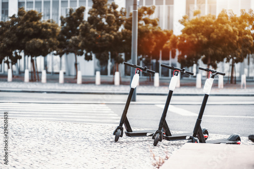 Electric urban transportation: three modern electric charged readies to ride e-scooter bikes with white accumulators above on the paving stone with the road and trees behind, Lisbon, Portugal