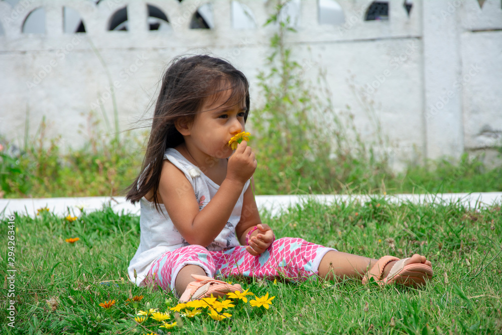 Sad little girl smelling flowers sitting on the grass Sad little girl smelling flowers sitting on the grass