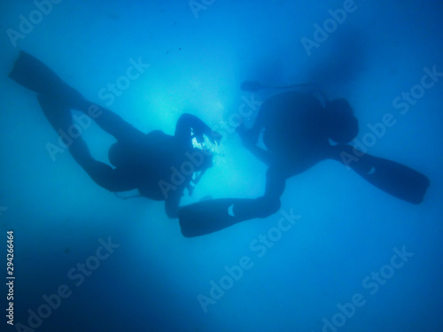 Two divers ascending to surface in hazy blue water