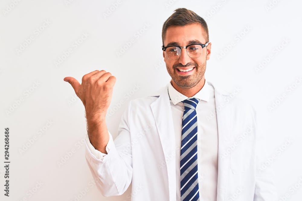 Young handsome therapist man over isolated background smiling with happy face looking and pointing to the side with thumb up. Young handsome therapist man over isolated background smiling with happy face looking and pointing to the side with thumb up.