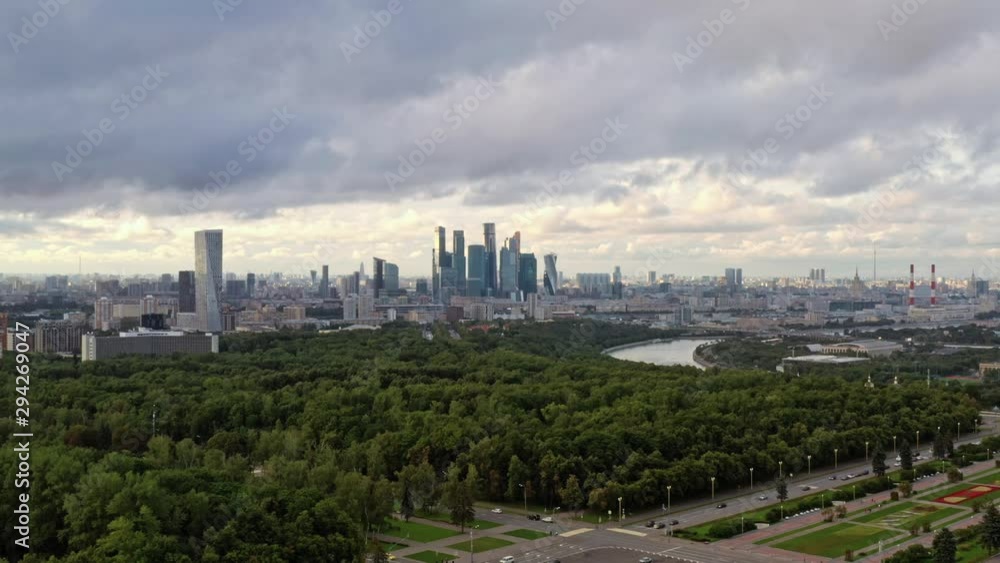 Aerial drone zoom in of Moscow Business Center and green forest park and residential buildings under cloudy sky. Drone shot of residential area and Moscow center Aerial drone zoom in of Moscow Business Center and green forest park and residential buildings under cloudy sky. Drone shot of residential area and Moscow center