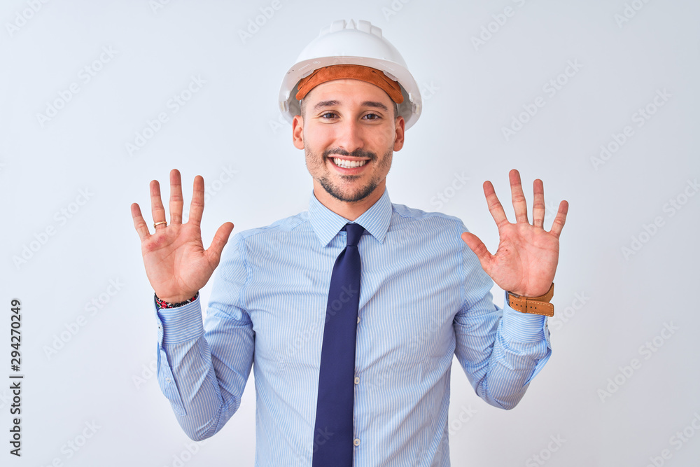 Young business man wearing contractor safety helmet over isolated background showing and pointing up with fingers number ten while smiling confident and happy.