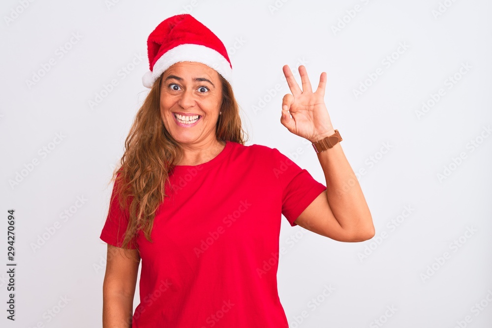 Middle age mature woman wearing christmas hat over isolated background smiling positive doing ok sign with hand and fingers. Successful expression. Middle age mature woman wearing christmas hat over isolated background smiling positive doing ok sign with hand and fingers. Successful expression.
