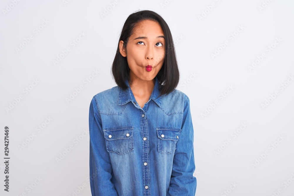 Young beautiful chinese woman wearing denim shirt standing over isolated white background making fish face with lips, crazy and comical gesture. Funny expression. Young beautiful chinese woman wearing denim shirt standing over isolated white background making fish face with lips, crazy and comical gesture. Funny expression.