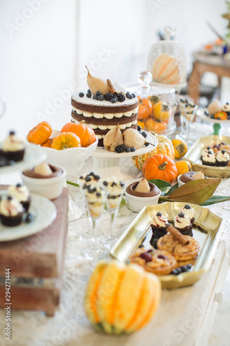 Sweet table. Halloween Wedding Luxor Decor. Chocolate cake with blackberries  blueberries  pears and cinnamon sticks. Cupcakes and tartlets with berries. Surrounded by orange pumpkins