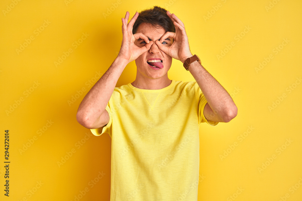 Teenager boy wearing yellow t-shirt over isolated background doing ok gesture like binoculars sticking tongue out, eyes looking through fingers. Crazy expression. Teenager boy wearing yellow t-shirt over isolated background doing ok gesture like binoculars sticking tongue out, eyes looking through fingers. Crazy expression.