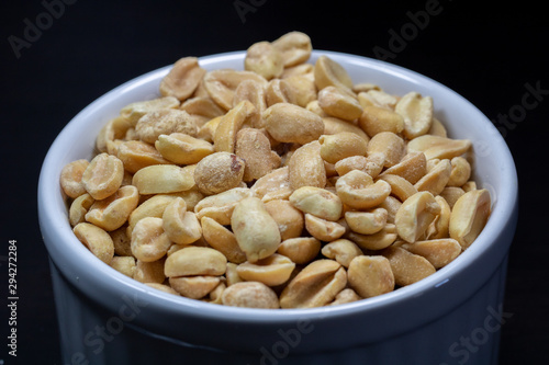 macro photography of shelled and salted peanuts in a white canister with black background
