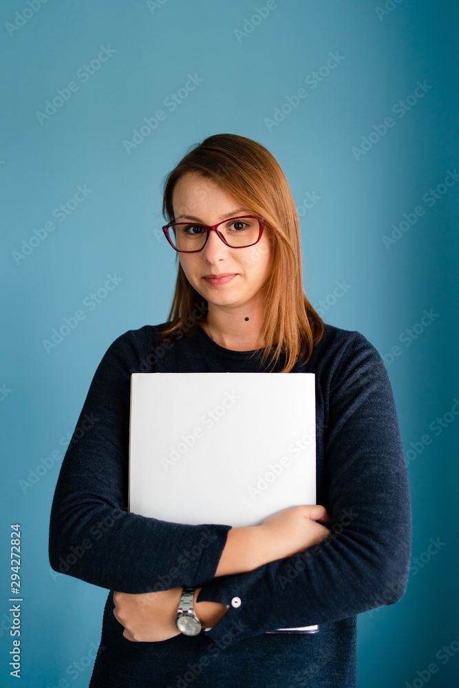 Portrait of young business woman with glasses secretary holding file folder job application in front of blue wall Portrait of young business woman with glasses secretary holding file folder job application in front of blue wall