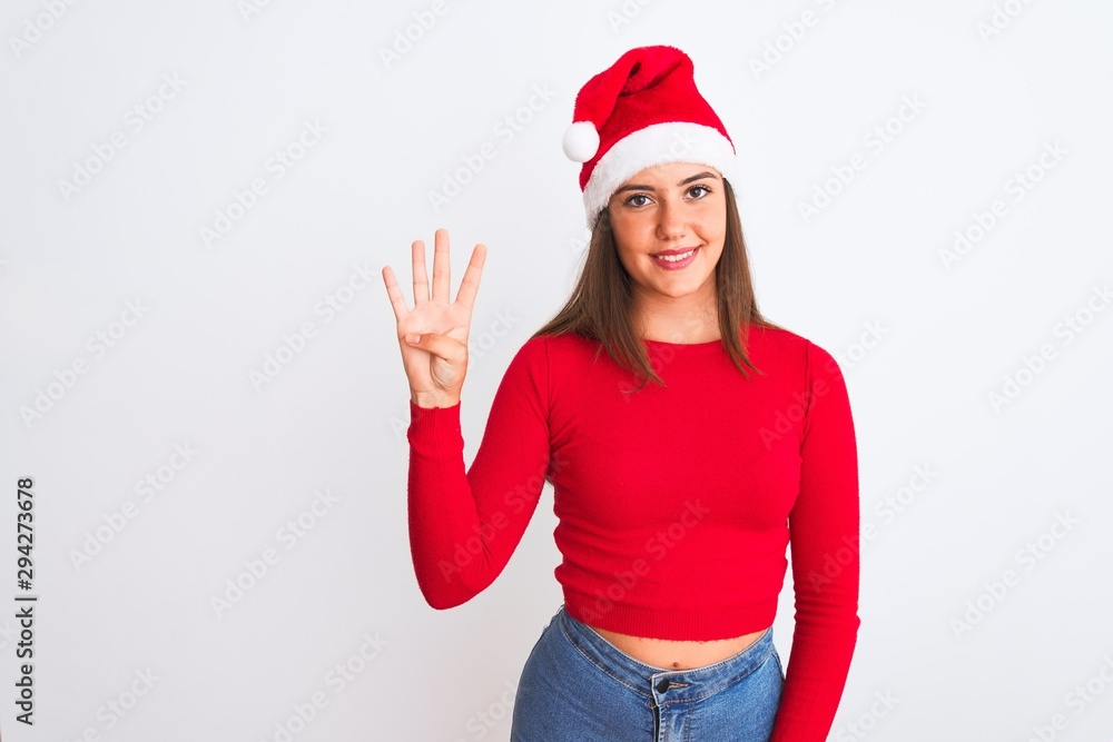 Young beautiful girl wearing Christmas Santa hat standing over isolated white background showing and pointing up with fingers number four while smiling confident and happy.