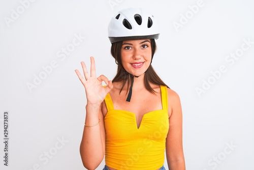Young beautiful cyclist girl wearing bike helmet standing over isolated white background doing ok sign with fingers, excellent symbol © Krakenimages.com