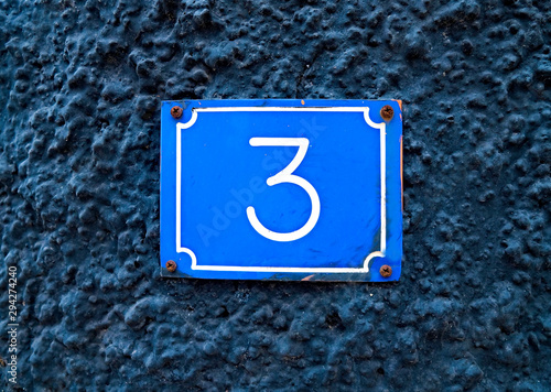 Number 3, three, on a blue plate on a murky dark blue background.