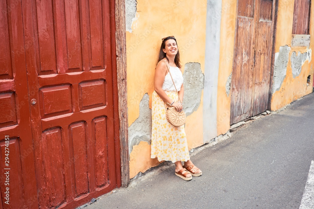 Fototapeta premium Beautiful girl leaning on orange wall, young friendly woman smiling happy on a sunny day of summer