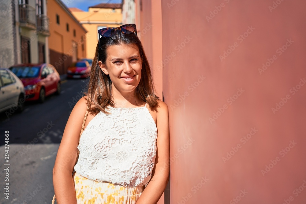 Fototapeta premium Beautiful girl leaning on orange wall, young friendly woman smiling happy on a sunny day of summer