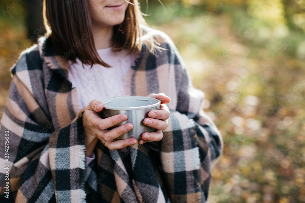 Girl in the autumn forest drinking tea from a thermos. The girl is in a great mood and happy Girl in the autumn forest drinking tea from a thermos. The girl is in a great mood and happy