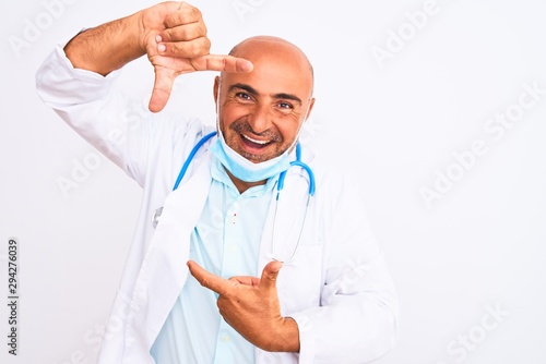 Middle age doctor man wearing stethoscope and mask over isolated white background smiling making frame with hands and fingers with happy face. Creativity and photography concept.