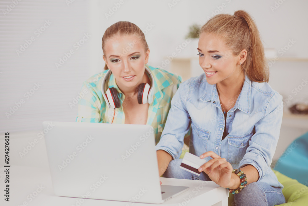 Happy relaxed young female friends doing online shopping through laptop and credit card at home Happy relaxed young female friends doing online shopping through laptop and credit card at home