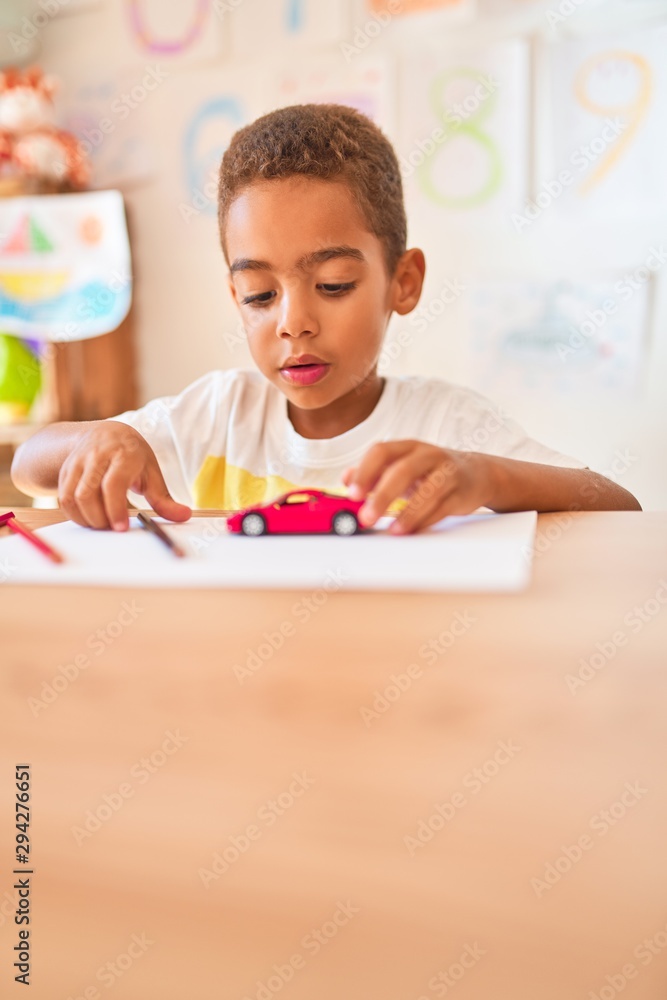 Beautiful african american toddler sitting drawing using paper and pencils on desk at kindergarten Beautiful african american toddler sitting drawing using paper and pencils on desk at kindergarten