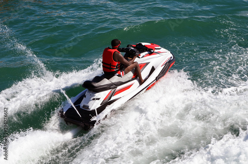 Angled overhead view of a man running waves on a speeding jet ski.