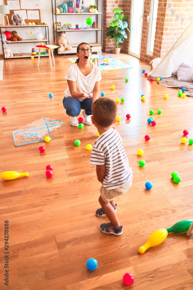 Fototapeta premium Beautiful teacher and toddler boy playing with colored small balls at kindergarten