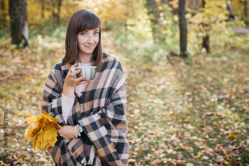 Girl in the autumn forest drinking tea with leaves in his hands. The girl is in a great mood and happy