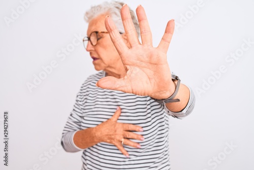 Senior grey-haired woman wearing striped navy t-shirt glasses over isolated white background covering eyes with hands and doing stop gesture with sad and fear expression. Embarrassed