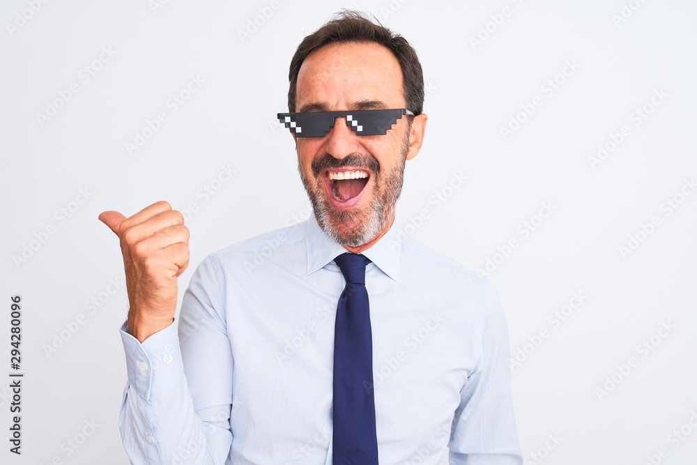 Middle age businessman wearing thug life sunglasses over isolated white background smiling with happy face looking and pointing to the side with thumb up. Middle age businessman wearing thug life sunglasses over isolated white background smiling with happy face looking and pointing to the side with thumb up.