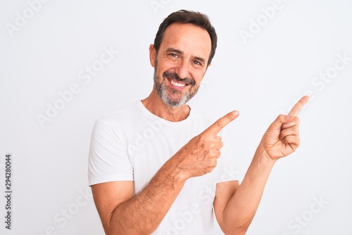 Middle age handsome man wearing casual t-shirt standing over isolated white background smiling and looking at the camera pointing with two hands and fingers to the side.