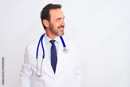 Middle age doctor man wearing coat and stethoscope standing over isolated white background looking away to side with smile on face, natural expression. Laughing confident.