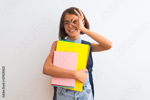 Beautiful student child girl wearing backpack glasses books over isolated white background with happy face smiling doing ok sign with hand on eye looking through fingers