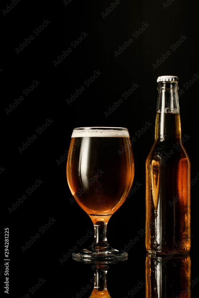 glass of beer with foam near bottle isolated on black glass of beer with foam near bottle isolated on black