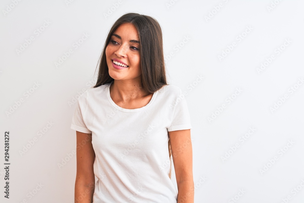 Young beautiful woman wearing casual t-shirt standing over isolated white background looking away to side with smile on face, natural expression. Laughing confident. Young beautiful woman wearing casual t-shirt standing over isolated white background looking away to side with smile on face, natural expression. Laughing confident.