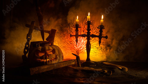 Scary orange pumpkin with carved eyes and a smile with burning candles and an ax photo