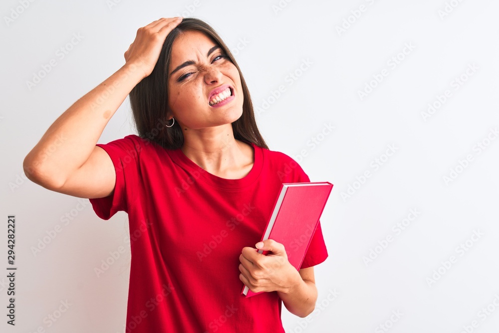 Young beautiful student woman holding red book standing over isolated white background stressed with hand on head, shocked with shame and surprise face, angry and frustrated Young beautiful student woman holding red book standing over isolated white background stressed with hand on head, shocked with shame and surprise face, angry and frustrated