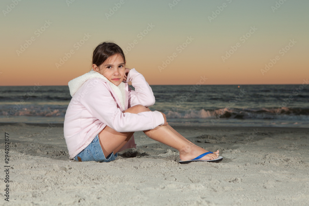 8 Year old girl sitting on beach at dusk