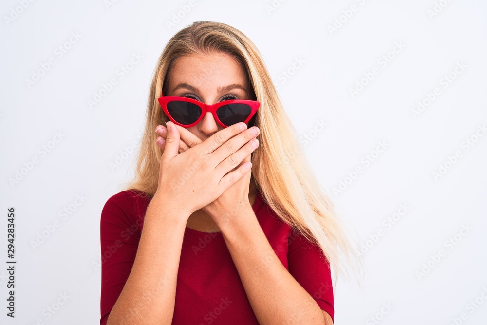 Young beautiful woman wearing red t-shirt and sunglasses over isolated white background shocked covering mouth with hands for mistake. Secret concept. Young beautiful woman wearing red t-shirt and sunglasses over isolated white background shocked covering mouth with hands for mistake. Secret concept.