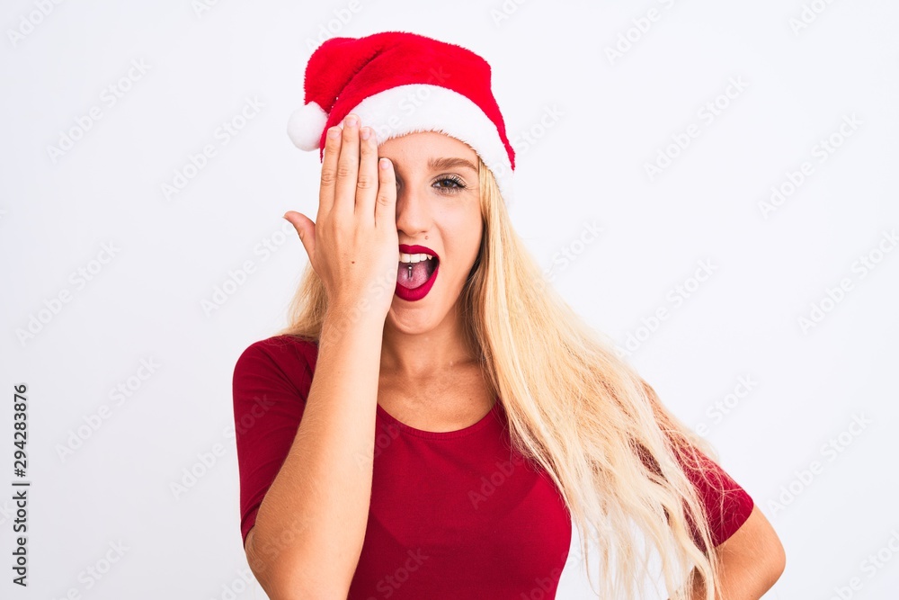 Young beautiful woman wearing Christmas Santa hat over isolated white background covering one eye with hand, confident smile on face and surprise emotion. Young beautiful woman wearing Christmas Santa hat over isolated white background covering one eye with hand, confident smile on face and surprise emotion.