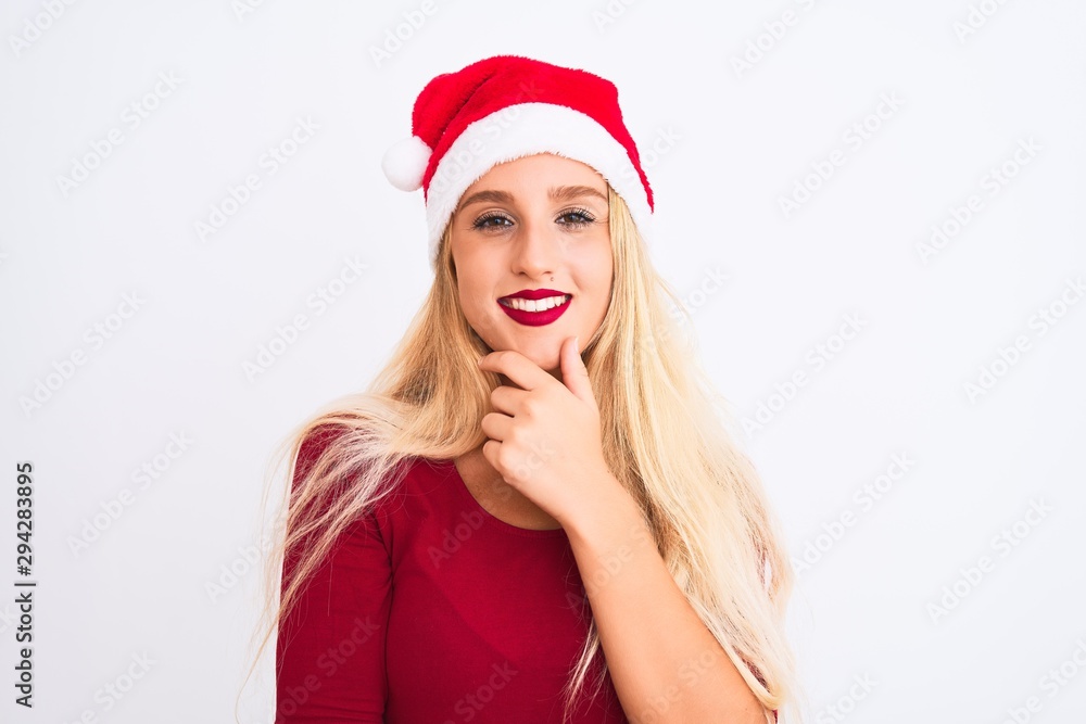 Young beautiful woman wearing Christmas Santa hat over isolated white background looking confident at the camera smiling with crossed arms and hand raised on chin. Thinking positive. Young beautiful woman wearing Christmas Santa hat over isolated white background looking confident at the camera smiling with crossed arms and hand raised on chin. Thinking positive.