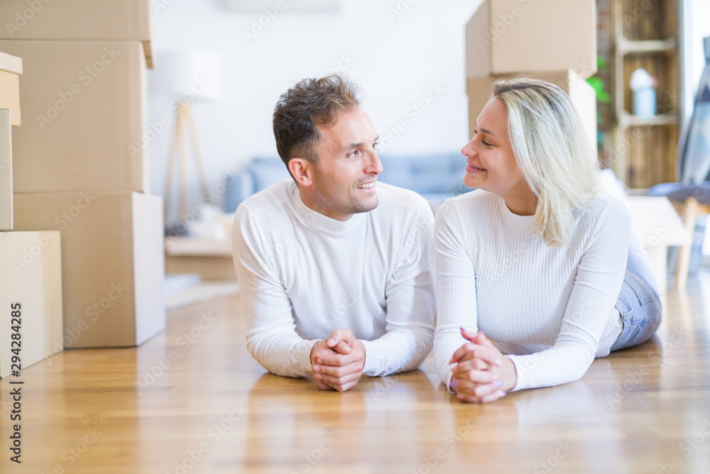 Fototapeta premium Young beautiful couple lying down on the floor at new home around cardboard boxes
