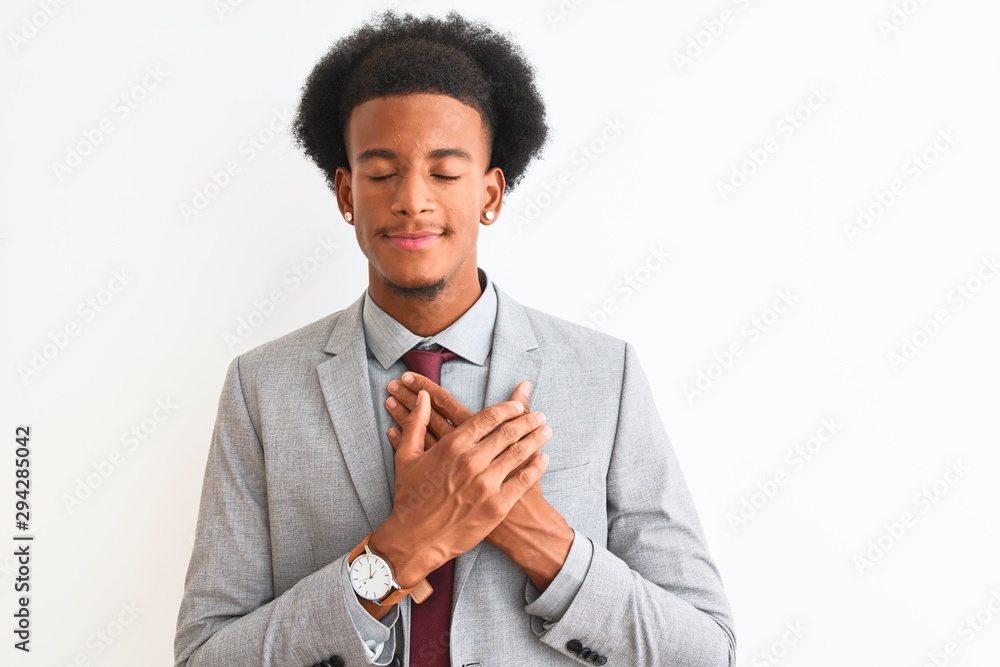 Young african american businessman wearing suit standing over isolated white background smiling with hands on chest with closed eyes and grateful gesture on face. Health concept. Young african american businessman wearing suit standing over isolated white background smiling with hands on chest with closed eyes and grateful gesture on face. Health concept.