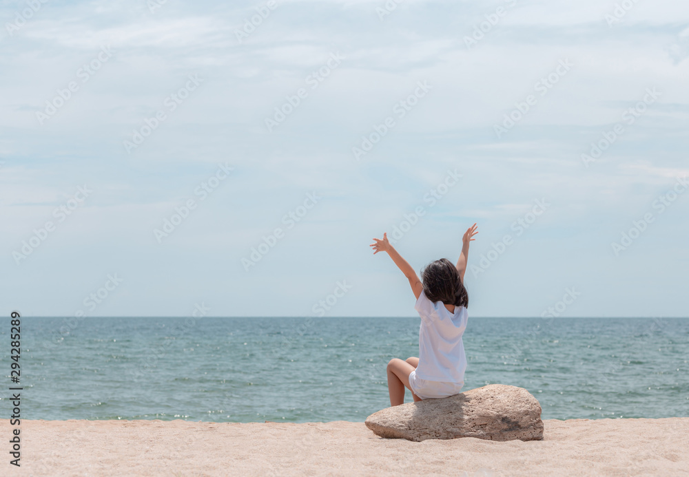 Happy little girl sitting enjoy with open arms and looking out to sea on the beach Happy little girl sitting enjoy with open arms and looking out to sea on the beach