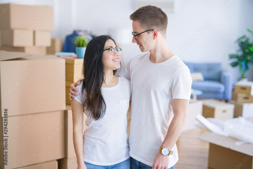 Fototapeta premium Young beautiful couple wearing glasses standing at new home around cardboard boxes