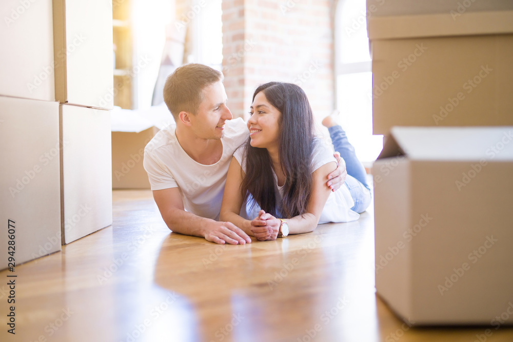 Young beautiful couple lying down at new home around cardboard boxes Young beautiful couple lying down at new home around cardboard boxes