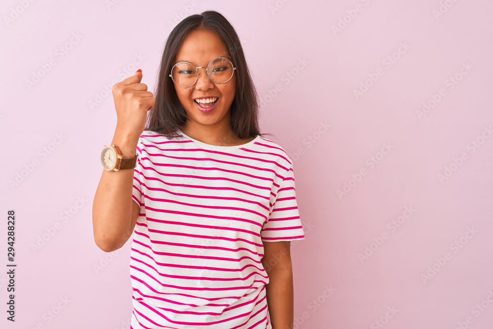 Young chinese woman wearing striped t-shirt and glasses over isolated pink background angry and mad raising fist frustrated and furious while shouting with anger. Rage and aggressive concept. Young chinese woman wearing striped t-shirt and glasses over isolated pink background angry and mad raising fist frustrated and furious while shouting with anger. Rage and aggressive concept.