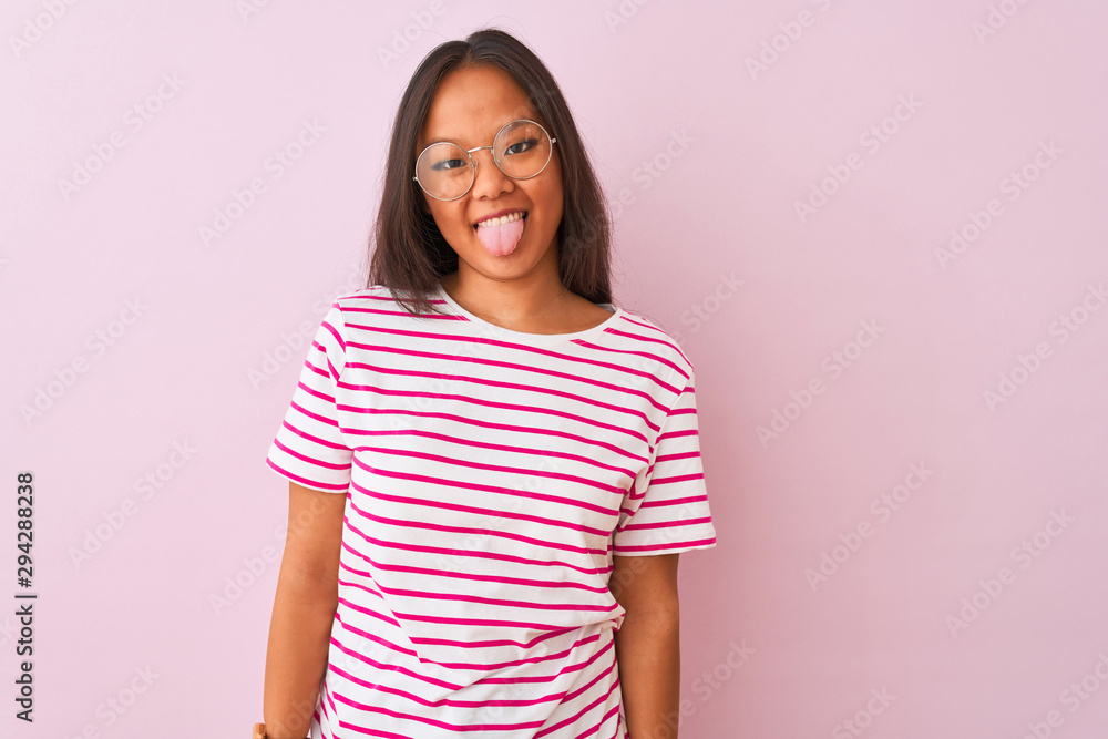 Young chinese woman wearing striped t-shirt and glasses over isolated pink background sticking tongue out happy with funny expression. Emotion concept. Young chinese woman wearing striped t-shirt and glasses over isolated pink background sticking tongue out happy with funny expression. Emotion concept.