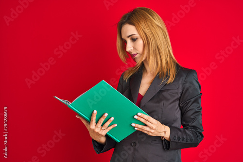 Young beautiful redhead businesswoman wearing suit reading book