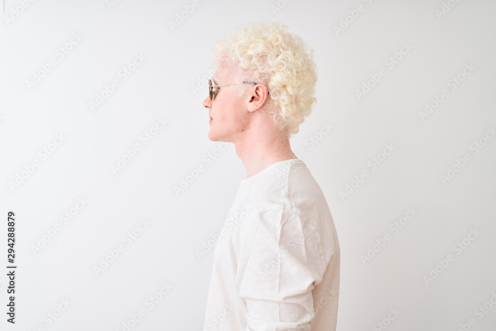 Young albino blond man wearing t-shirt and sunglasses over isolated white background looking to side, relax profile pose with natural face with confident smile.
